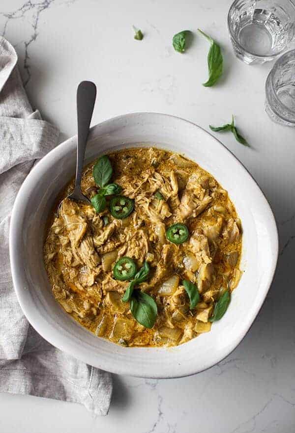 basil curry in a white bowl with a marble countertop and fresh basil leaves around it