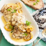 Grilled Mahi Mahi recipe with a lemon butter sauce with sliced lemons on top on a white plate with a turquoise background and a white and blue napkin on the side