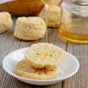 Light and Fluffy Paleo biscuits on a white plate with honey being drizzled on top on a wood table with a jar of honey in the background