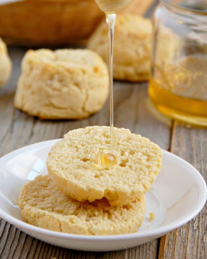 Light and Fluffy Paleo biscuits on a white plate with honey being drizzled on top on a wood table with a jar of honey in the background