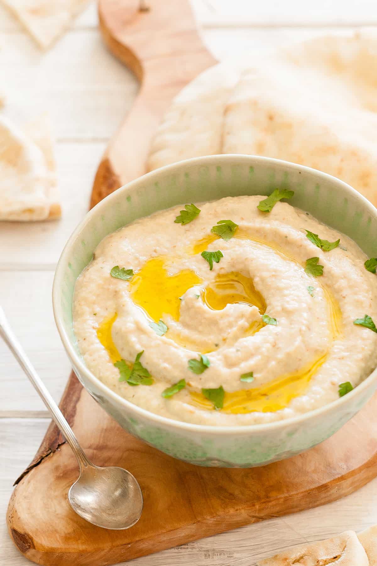 Keto baba ganoush in a bowl on a wood organic board with a spoon next to it.