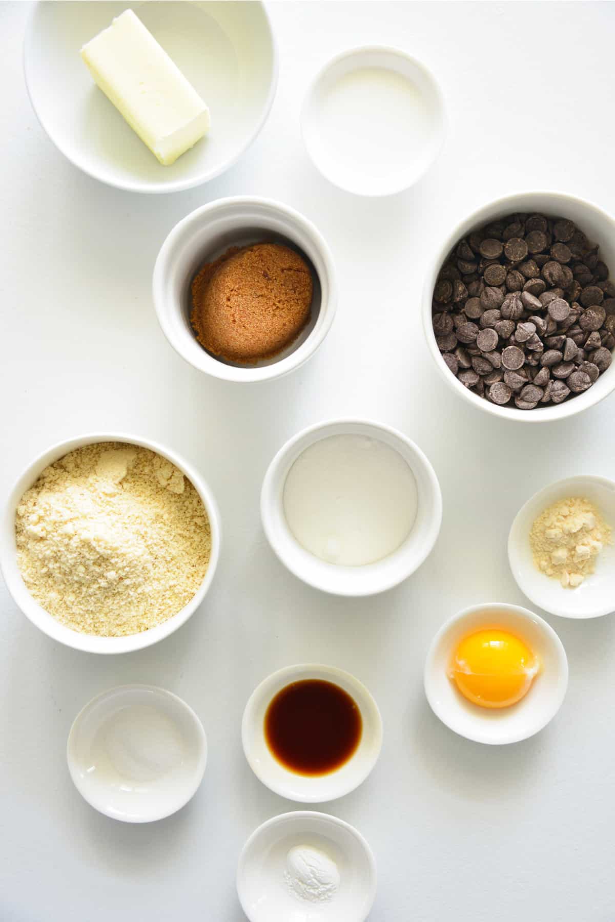 Ingredients in white bowls - butter, keto brown sugar (such as Swerve Brown or Besti Monk Fruit Allulose Blend Brown), granulated or crystallized monkfruit/allulose blend (such as Besti Monk Fruit Allulose Blend Crystallized), egg yolk, whole milk, vanilla, almond flour, coconut flour, salt, baking soda, stevia-sweetened chocolate chips