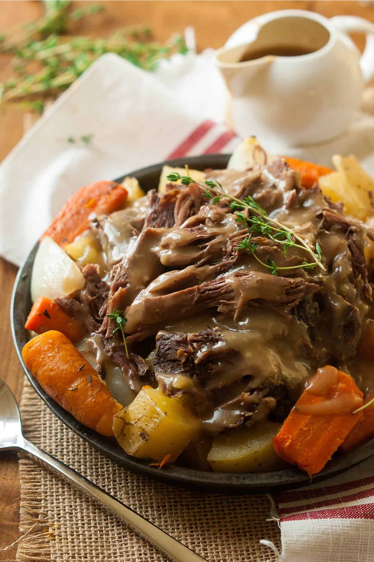 Crock pot roast with potatoes and carrots in a gray bowl on a textured cloth and a white and red napkin
