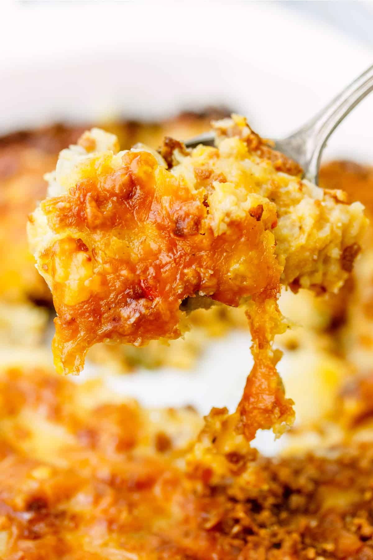 A large scoop of gluten-free cheesy potatoes held in front of the camera with the pan full of potatoes in the background.