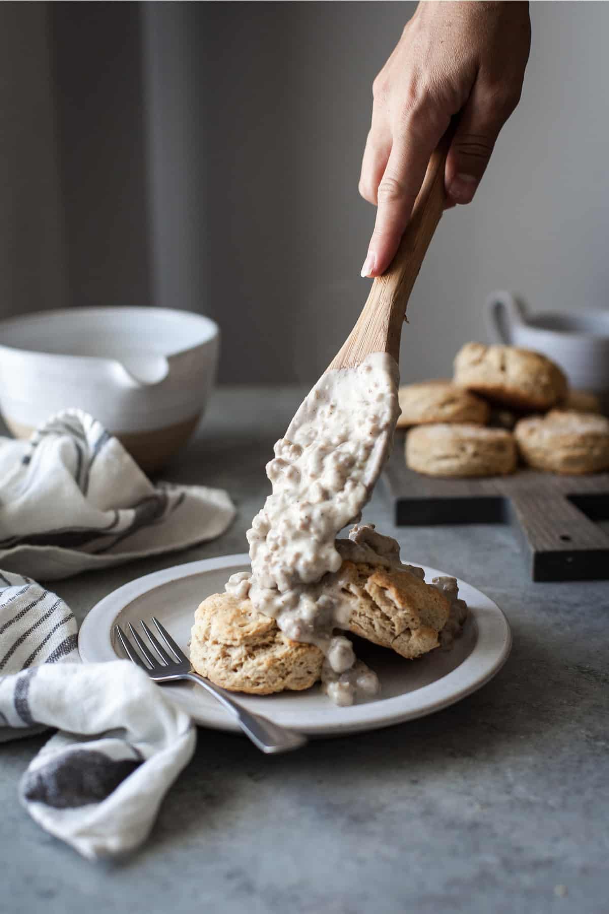 Healthy biscuits and gravy on a white plate with a fork and a white napkin with a blue stripe on a gray table.