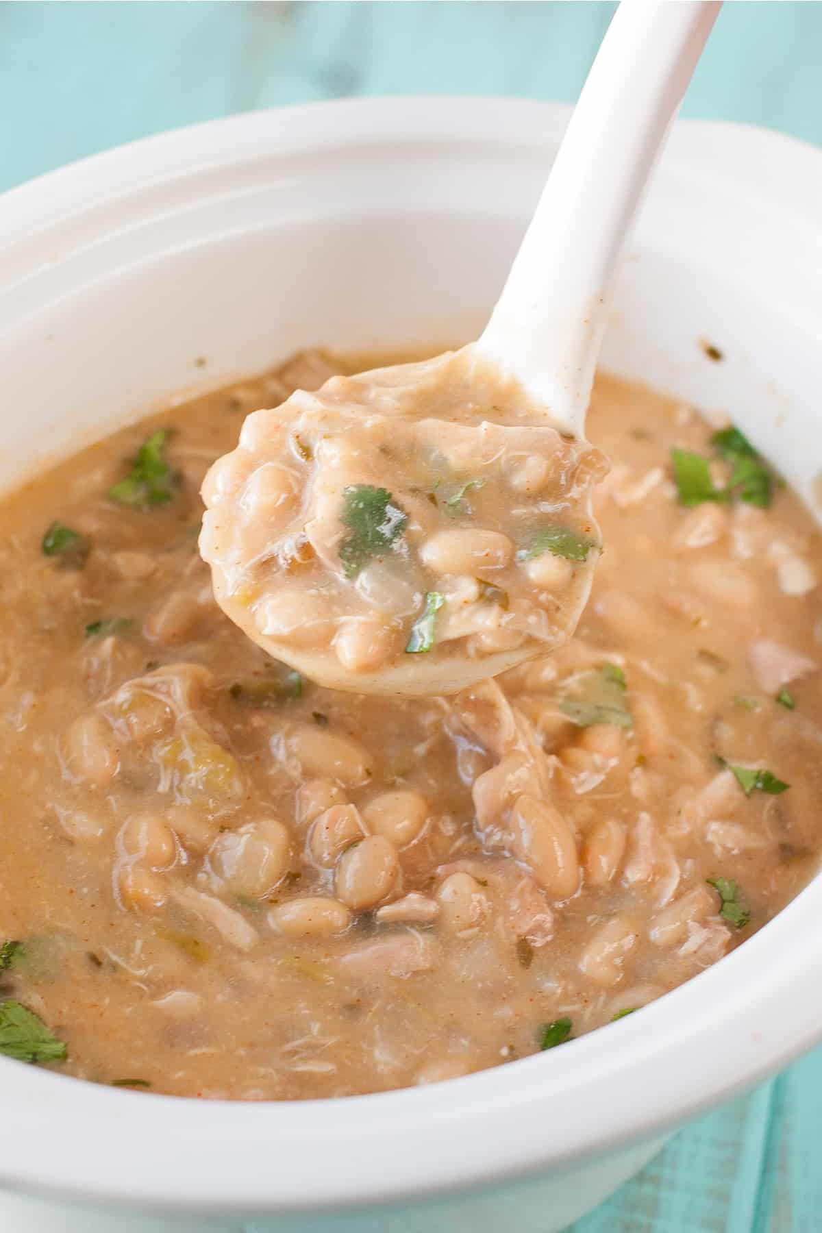 Healthy crockpot white chicken chili in a white slow cooker with a white serving spoon coming out of it.