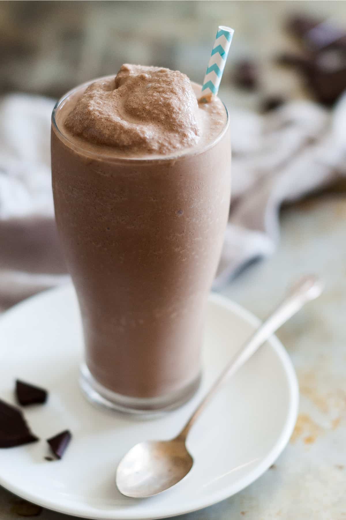 Healthy frosty on a white plate with a spoon and chocolate shavings on a gray table.
